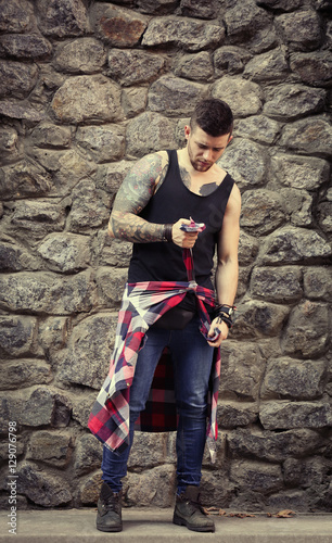 Young tattooed man posing on stone wall background