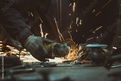Cutting a piece of steel tube pipe with an angle grinder on a work table with details of other industrial tools in the foreground photo