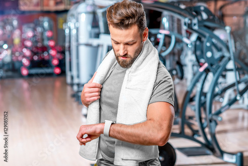 Lifestyle portrait of handsome muscular man looking at the smart watch after the exercise in the sport gym