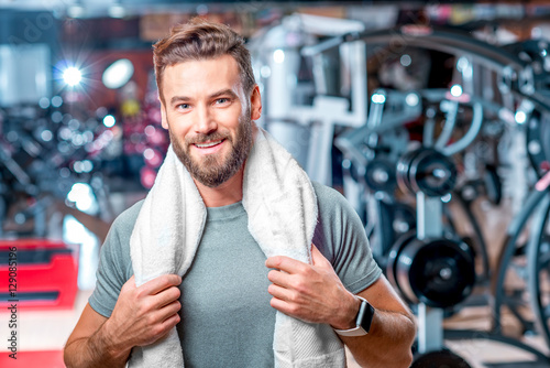 Lifestyle portrait of handsome muscular man standing with towel after the training in the sport gym