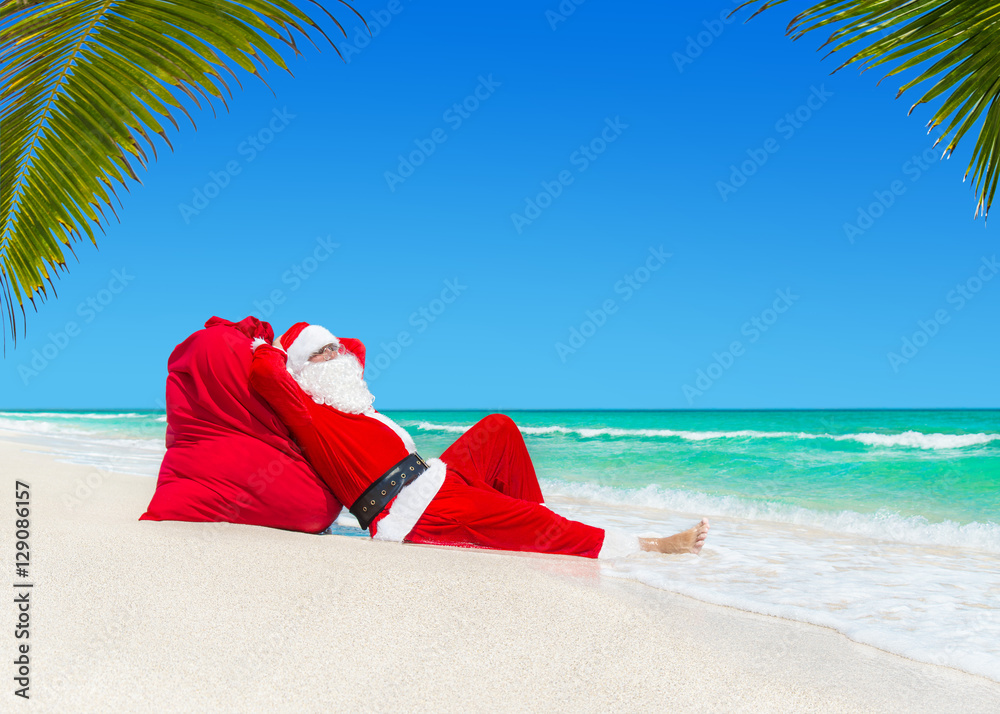 Santa Claus sunbathing on Christmas gifts sack at ocean palm beach Santa Claus sunbathing on Christmas gifts sack at ocean palm beach