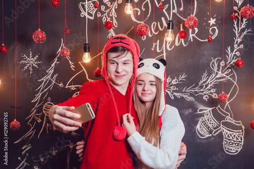 Happy couplein funny hats standing hugging and make selfie on a dark background with Christmas pattern. New year. photo