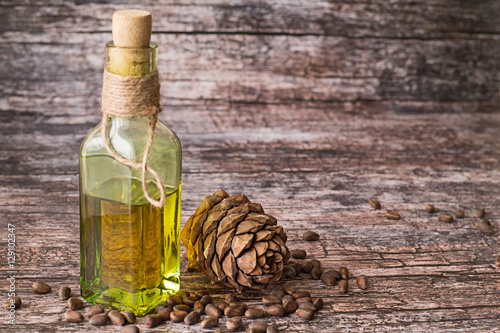 
 Cedar oil.   Cedar oil in a glass bottle and a cedar cones with nuts on a brown wooden background. photo