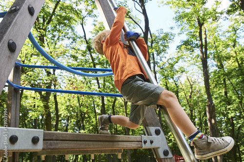 Little child boy climbing rope on the playground outdoors