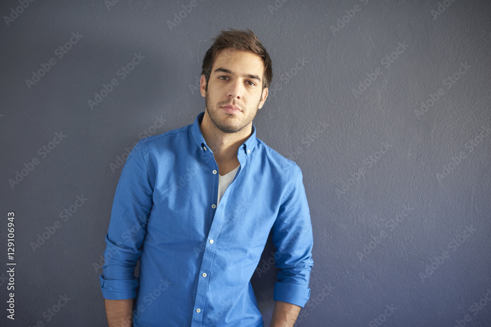 Confident young man portrait. Shot of a handsome man wearing casual clothing and looking at camera while standing at grey wall.