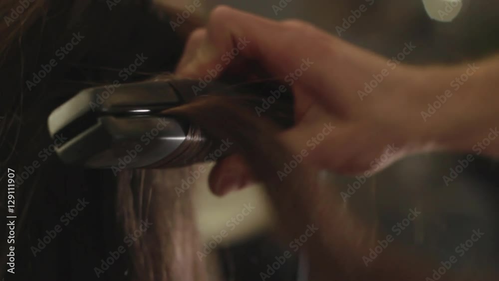 Hairdresser makes hair styling by using curling in a beauty salon for girl