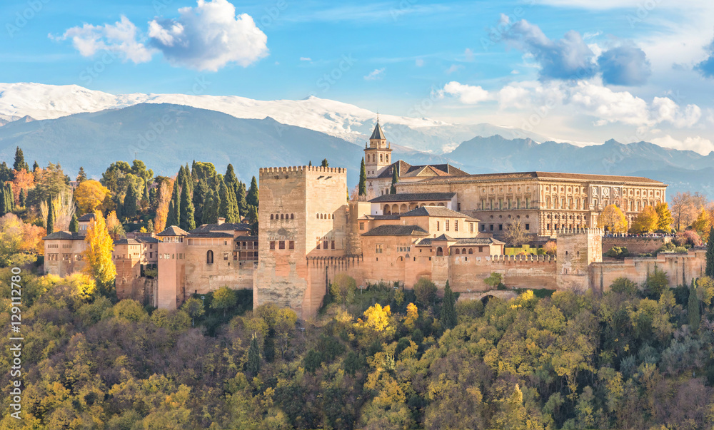 Alhambra - medieval Moorish fortress surrounded by yellow autumn trees with snow mountains on background, Granada, Andalusia, Spain