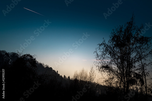 A cold sunrise with a starting airplane in the blue sky