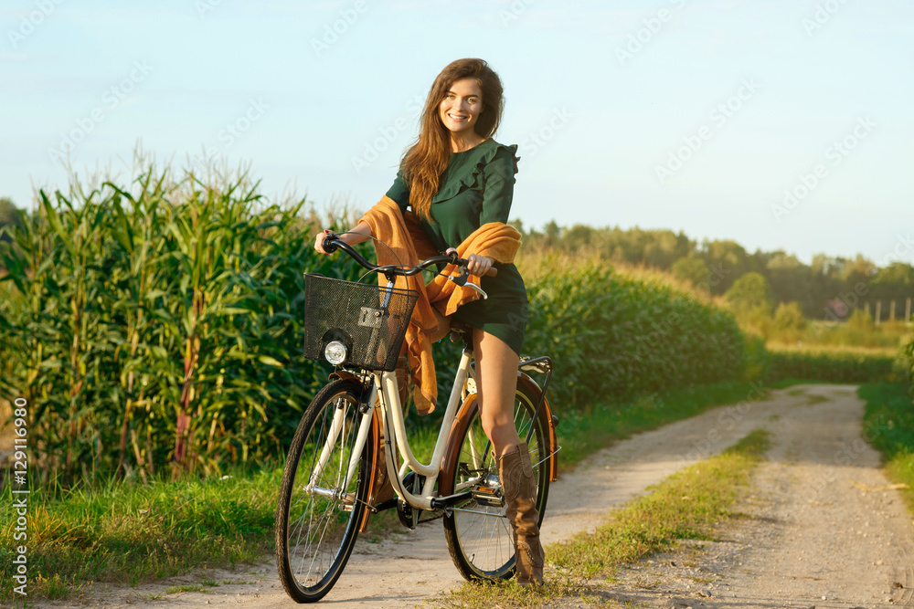 Fototapeta premium Woman is cycling by the country road in the cornfield