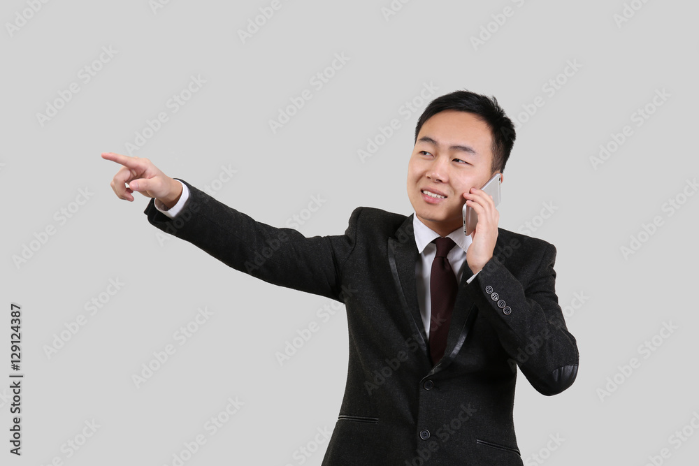 Handsome Asian man pointing at something while talking by mobile phone, on light background Handsome Asian man pointing at something while talking by mobile phone, on light background