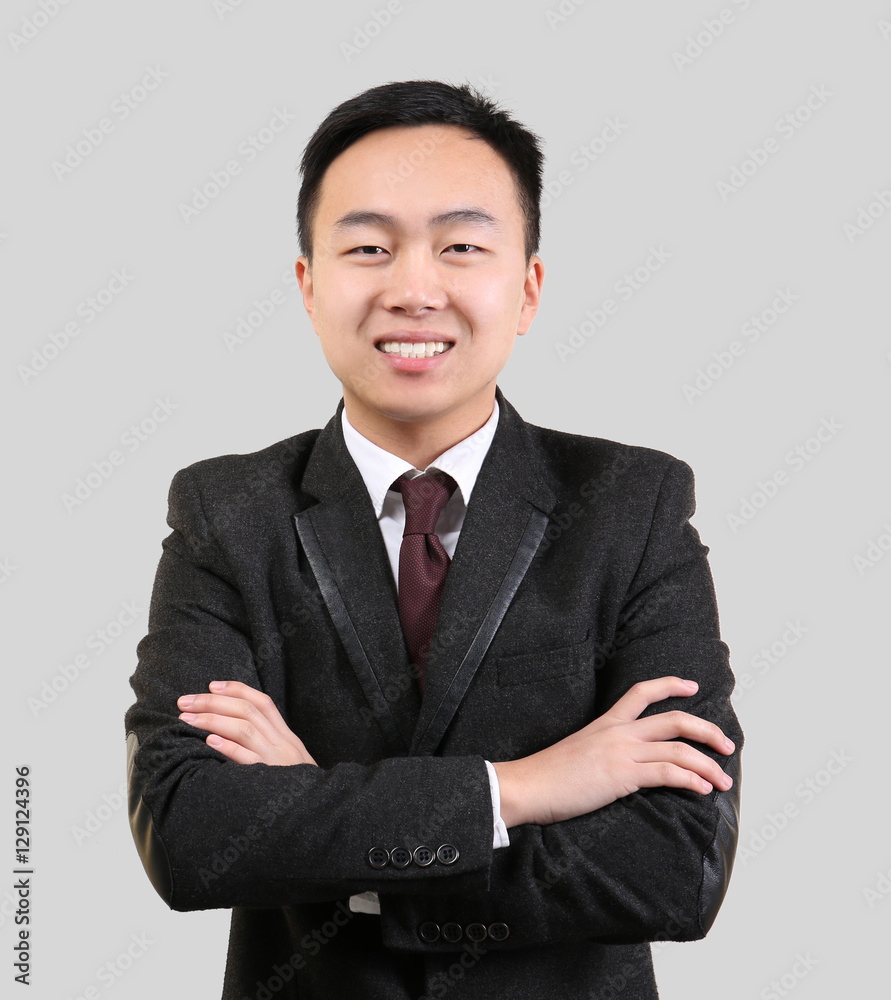 Handsome Asian man with crossed arms on light background