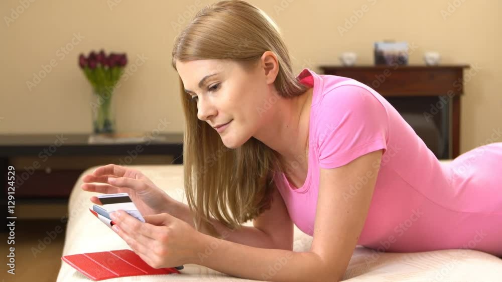 Beautiful attractive young woman lying on sofa and buying online with credit card on black tablet.