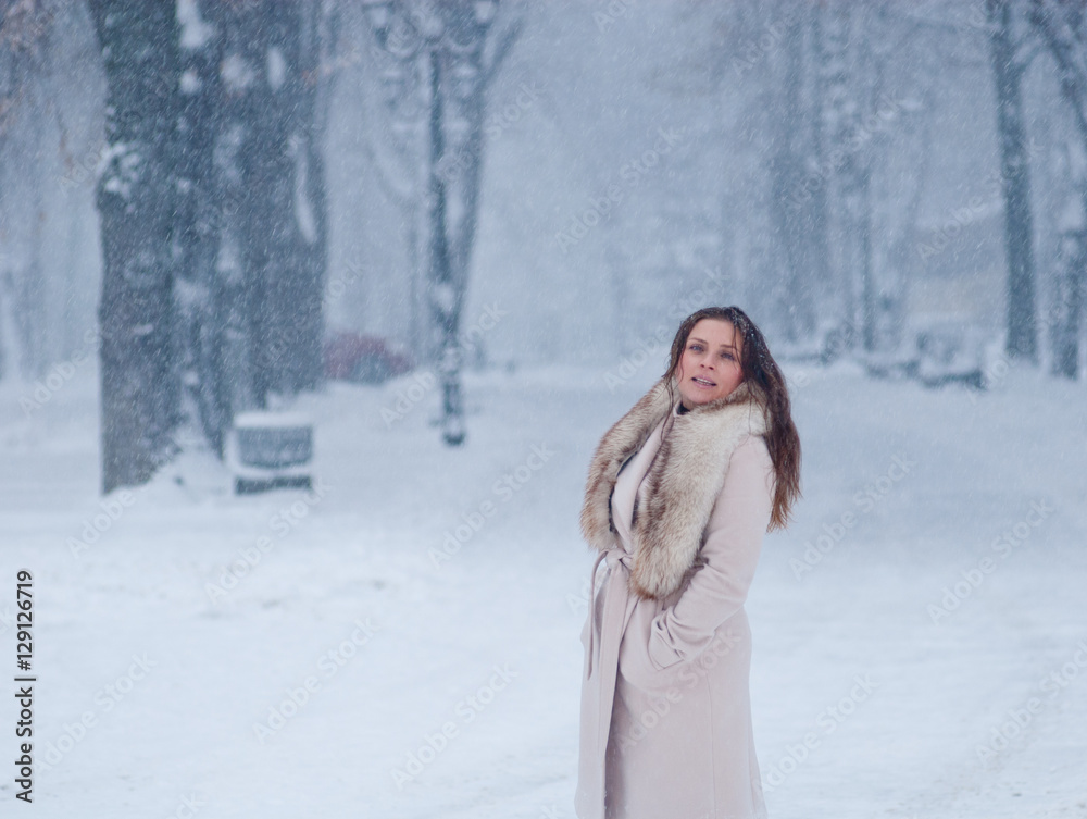 Winter portrait of a woman in white coat during snowfall in a park Winter portrait of a woman in white coat during snowfall in a park