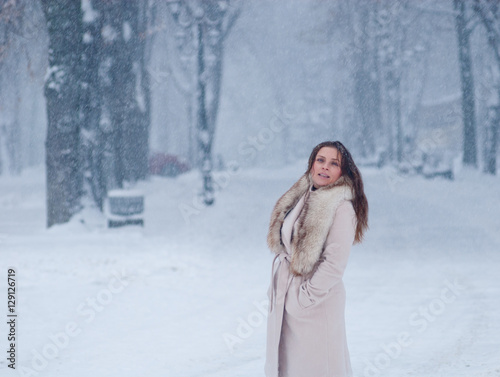 Winter portrait of a woman in white coat during snowfall in a park