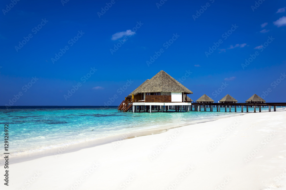 Typically Maldivian Landscape with turquoise ocean, blue sky, white sand beach and beach villas Typically Maldivian Landscape with turquoise ocean, blue sky, white sand beach and beach villas