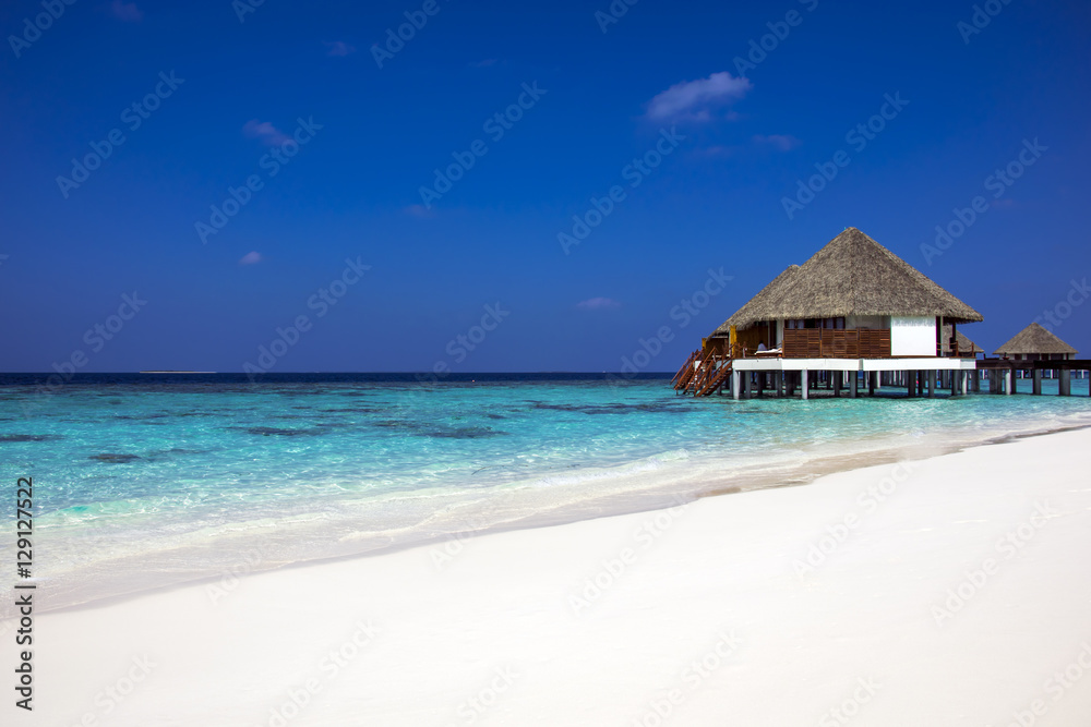 Typically Maldivian Landscape with turquoise ocean, blue sky, white sand beach and beach villas