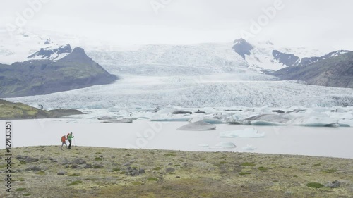 Iceland hiking travel people trekking by glacier. People by glacier and glacial lagoon / lake of Fjallsarlon  Vatnajokull National Park. Couple visiting Icelandic nature. RED EPIC  SLOW MOTION. photo