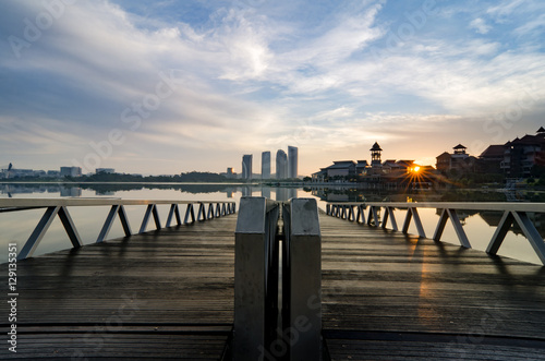 beautiful morning at lakeside. building reflection on the lake surface, soft and dramatic cloud with colorful on the sky. wooden jetty and soft look on the lake surface. © amirul syaidi