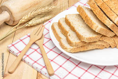 Sliced wholemeal bread on white plate with wheat ears on wooden table background, Closed up photo