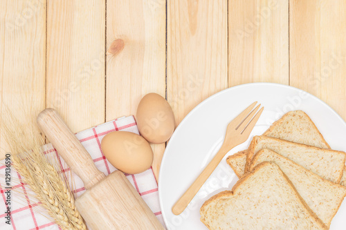 Sliced wholemeal bread on white plate with wheat ears and egg on wooden table background, Top view with copy space and text. photo