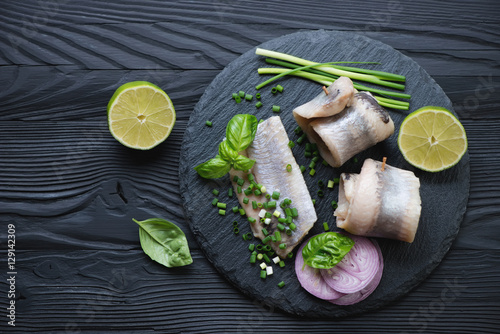 Stone slate tray with herring fillet rolls, black wooden surface