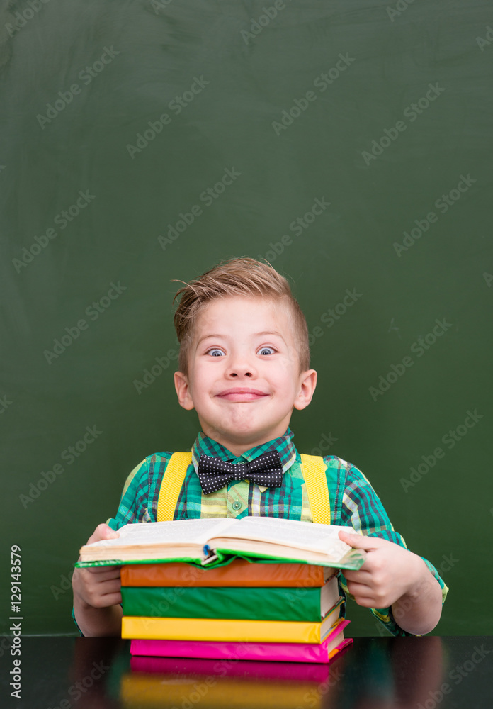 Funny boy reading a book near empty green chalkboard