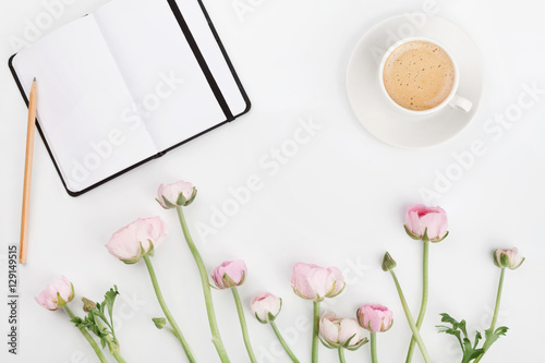 Beautiful spring Ranunculus flowers, empty notebook and cup of coffee on white desk from above. Greeting card. Breakfast. Pastel color. Clean space for text. Flat lay style.