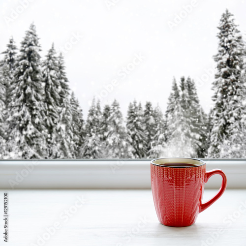 Coffee cup on a window sill. In the background, a beautiful winter forest in snow