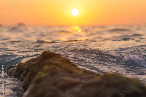 sea wave and rock close up at sunset time with red  orange sun reflection on the water. nature abstract blurred background. Phuket island, Thailand