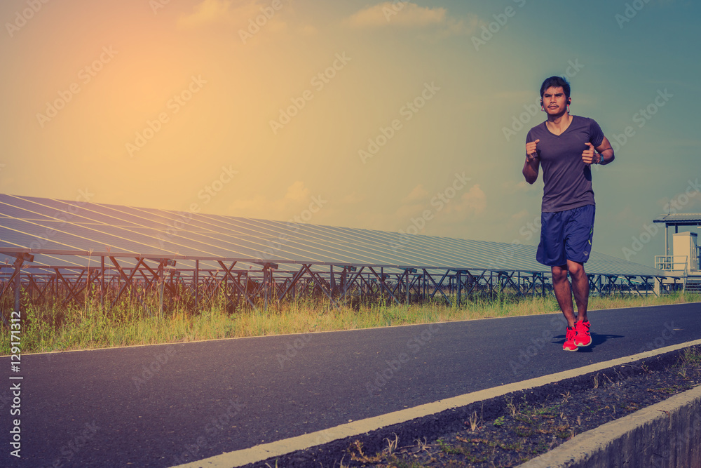 handsome man running on road with solar power plant in morning ;Healthy lifestyle with green energy
