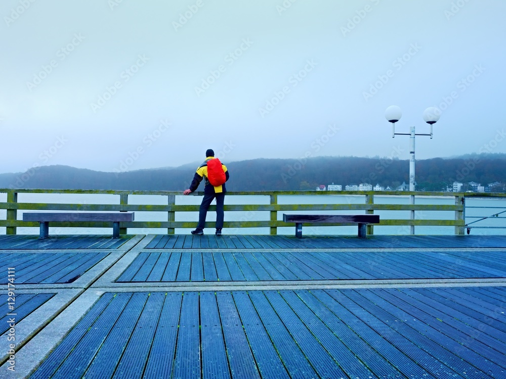 Tourist in autumn mist on wooden pier above sea. Depression, dark  atmosphere