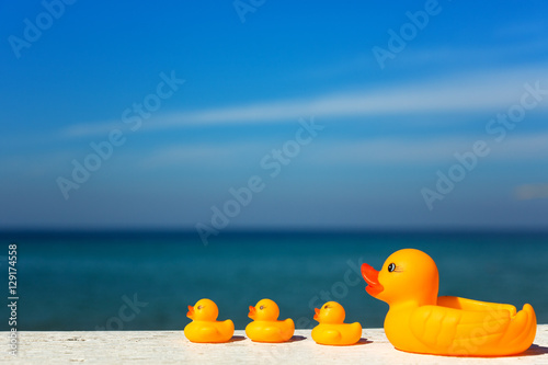 Baby bath ducks, on top of the white wooden table, against the sea.