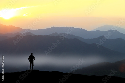 Climber standing the top of mountain in sunset background.