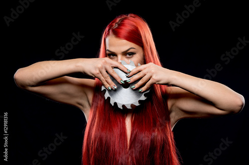 Portrait of beautiful girl with circular saw blade. Bretty naked woman, long red hair,  nude body, sawblade, dark background. Female and sharp stainless steel disc photo