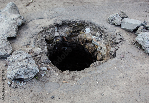 Broken manhole without cover in asphalt surface photo