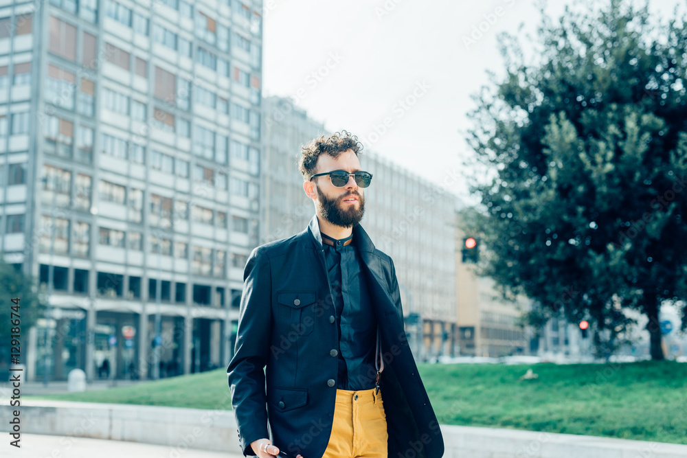 Young handsome caucasian bearded businessman strolling outdoor in the street, overlooking pensive wearing sunglasses - business, thoughtful, serious concept Young handsome caucasian bearded businessman strolling outdoor in the street, overlooking pensive wearing sunglasses - business, thoughtful, serious concept