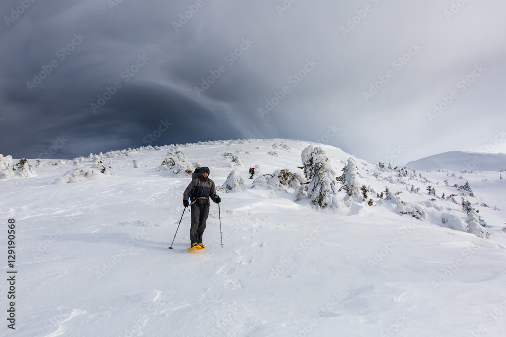 Man hiking in winter mountains before thunderstorm