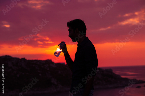 Profile of man silhouette drinking water from a bottle at sunset