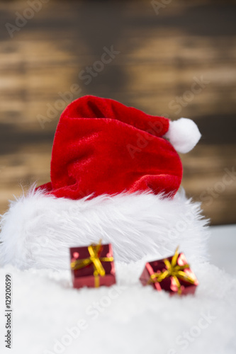 Santa Claus cap hat laying on snow with beautiful red christmas ornament on wooden background
