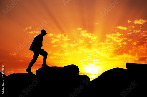 Silhouette of a man climbing on top of a mountain againt sunrise