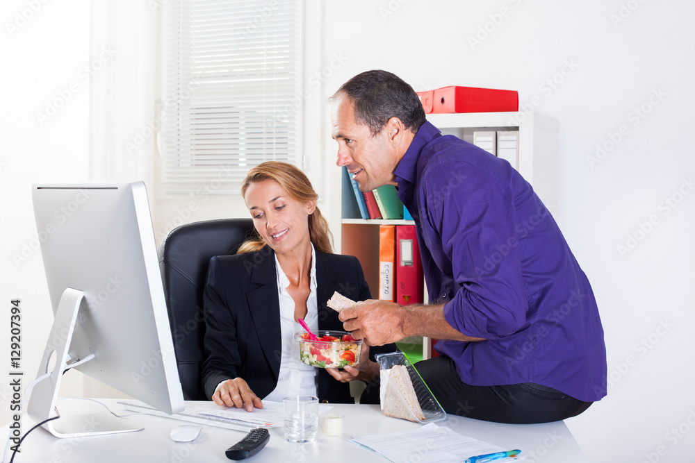 Obraz premium couple souriant au bureau qui mange en travaillant