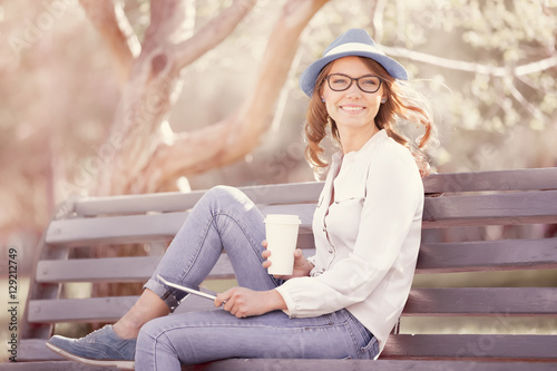 Sitting on the bench / A happy young student with a tablet pc and a disposable coffee cup sitting on the bench in a summer park. 