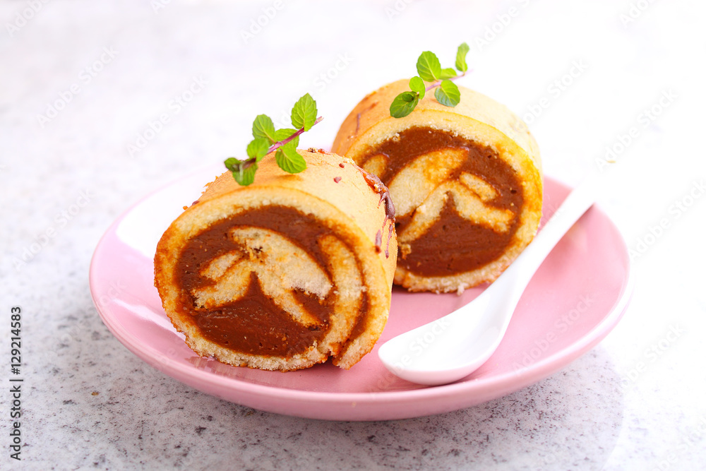 Swiss roll with condensed milk in a pink plate decorated with mint Swiss roll with condensed milk in a pink plate decorated with mint