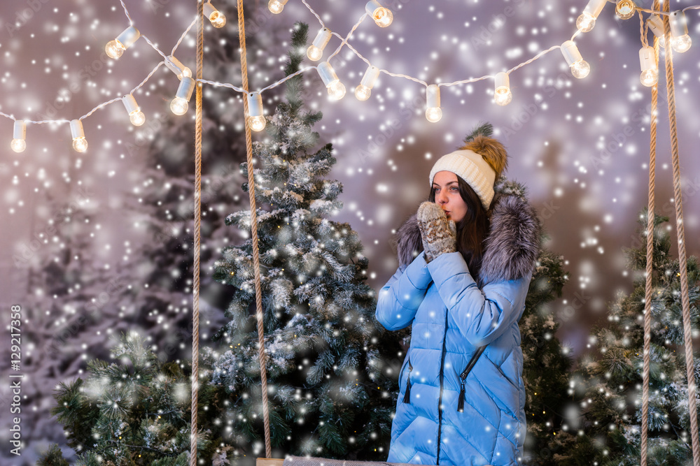 Female in blue down jacket warming hands in mittens under the fl Female in blue down jacket warming hands in mittens under the fl