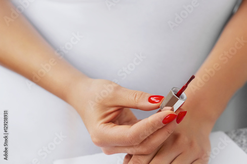 Woman hands - nail polish on light background. Girl holding nail polish brush in her hand. She painting her nails in red colour
