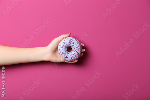 Female hand holding sweet donut on pink background
