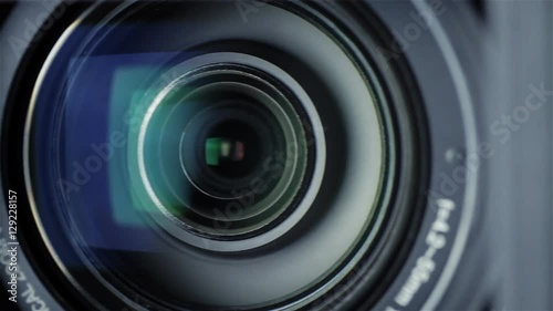 Closeup shot of a professional video camera while it's lens is zooming. The camera is turning towards the audience.