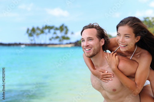 Beautiful healthy young people having fun. Multiracial piggyback couple on beach travel vacation in Caribbean destination. Happy smiling man piggybacking Asian woman.