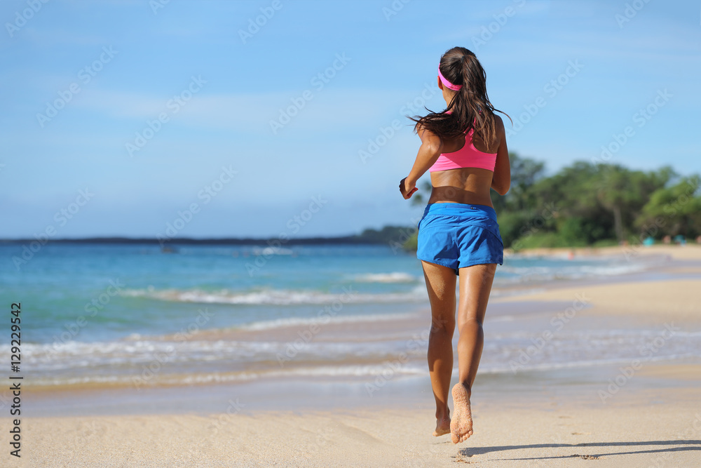 Woman runner running barefoot on sand at beach. Female athlete with slim legs jogging away, view from the back, on tropical travel destination.