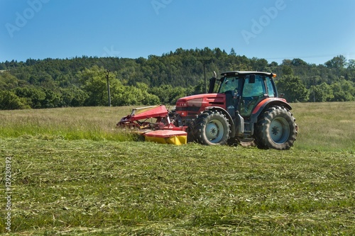 Agricultural work. Red tractor mowing the meadow, Czech Republic. Farmer harvested hay. 